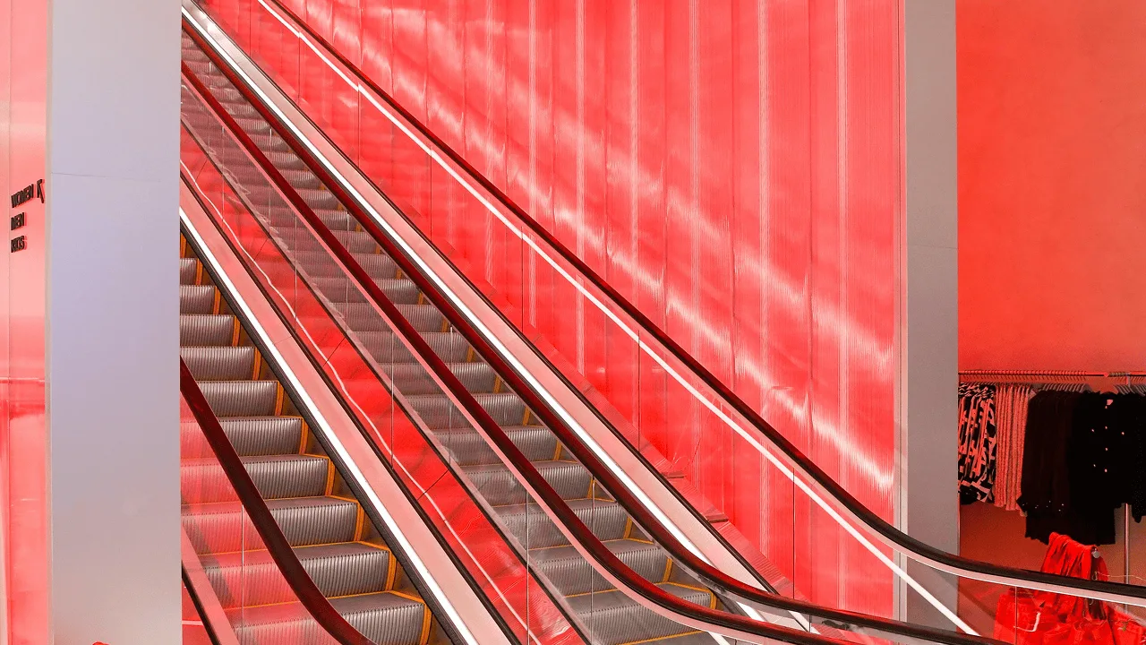 The escalator at the Times Square flagship climbing beside a tall ribbed wall backlit in deep red