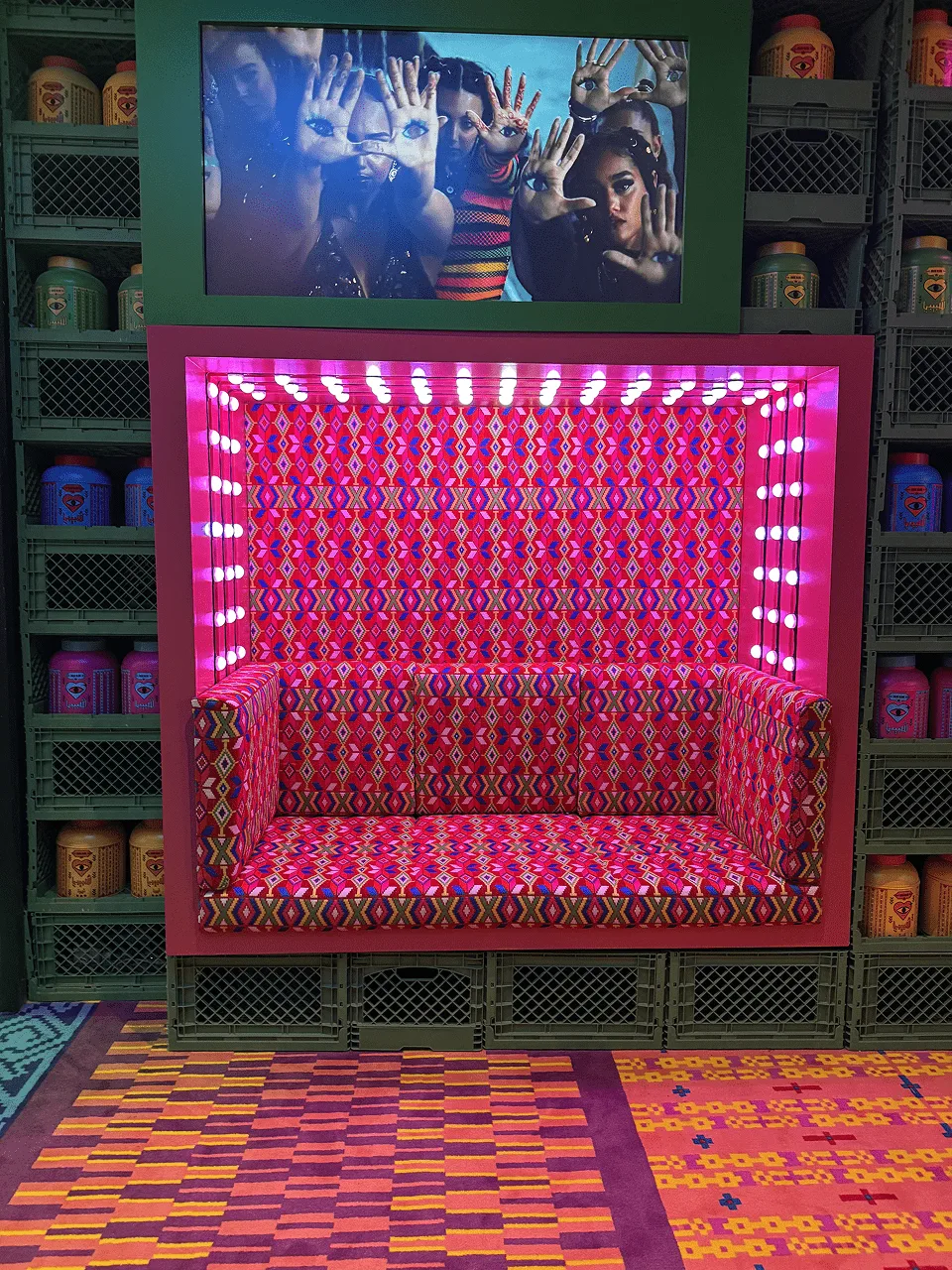 A pink bench set inside an infinity mirror frame studded with lights, a screen above it and crates stacked either side