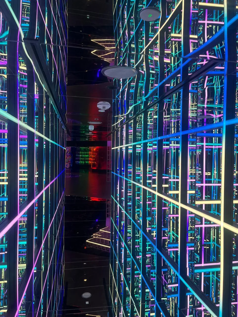 Mirror maze lit with green, blue and pink neon lines repeating away into the reflections