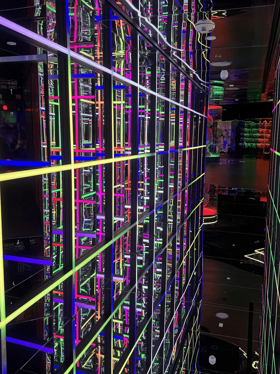 The same mirror maze from further in, brighter neon grids on the left and the game floor visible beyond