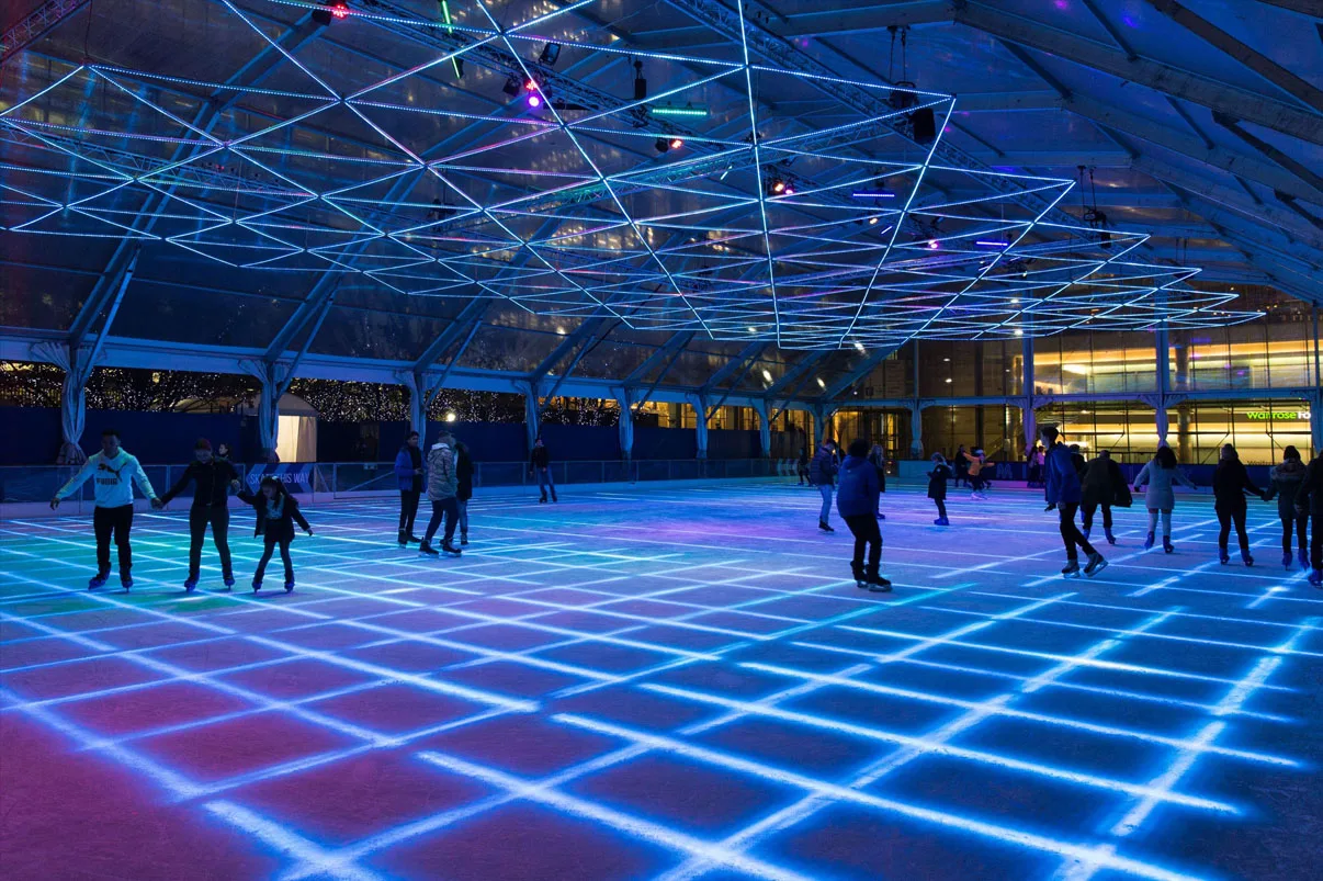 The rink from a near corner, a bright cyan grid running over a red and blue wash with skaters spread across it