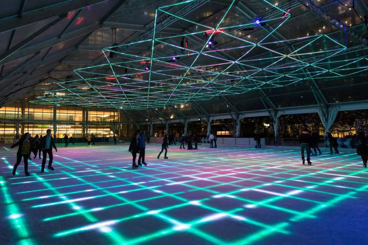 Teal and green lines gridding the ice, skaters over at the far barrier and Christmas lights strung beyond it