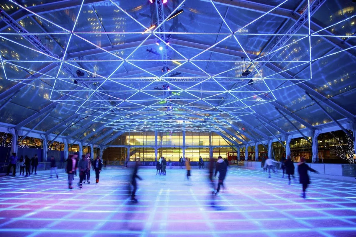 Mid rink under a violet and blue grid, blurred skaters mid stride and the lit office frontage behind them