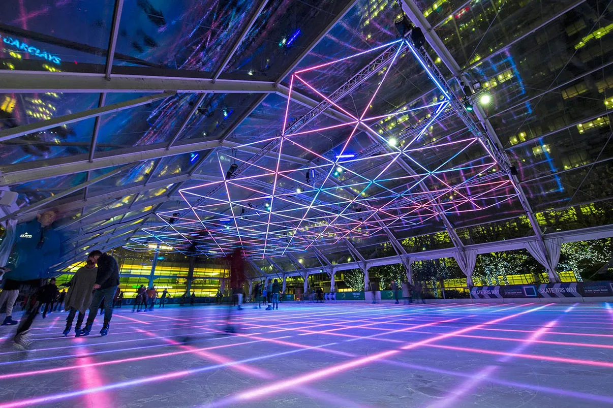 From beside the barrier, pink and magenta lines fanning across the ice with the canopy trusses lit to match