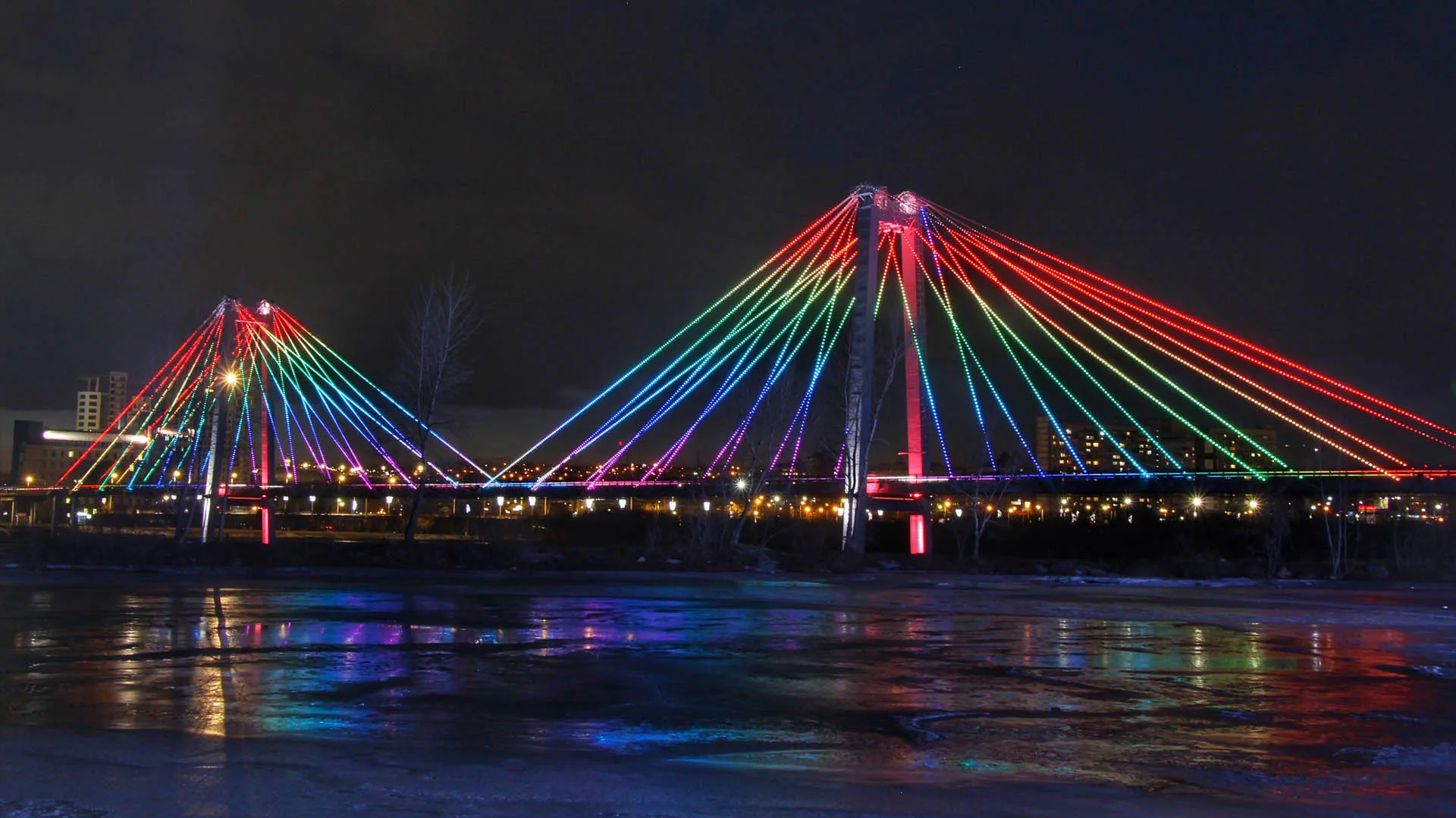 The span seen across the frozen river, cables banded in red, green and blue above the lights of the far bank