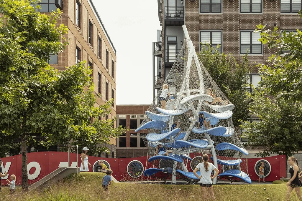 The outdoor climber in white and blue beside a brick apartment block, a child running across the grass below