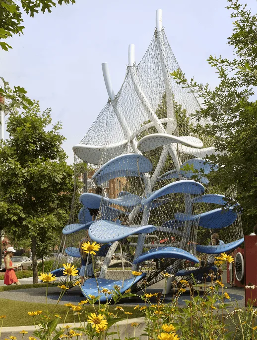 The outdoor sculpture head on, white net peaks against a pale sky, yellow sunflowers filling the foreground