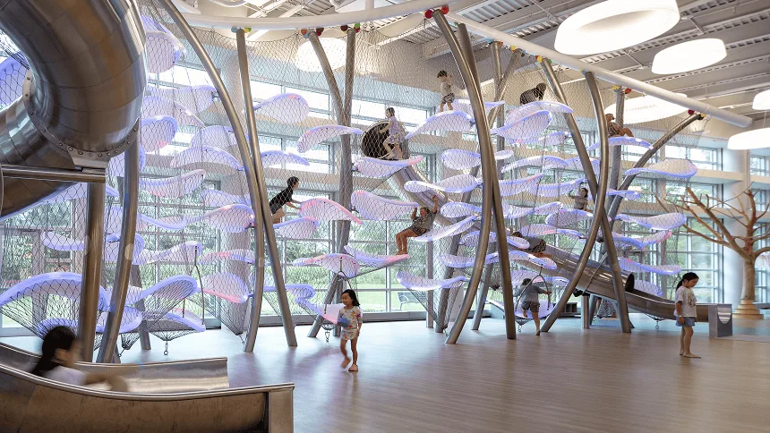 Wide view of the indoor climber lit lilac, children spread across the platforms while others cross the timber floor below