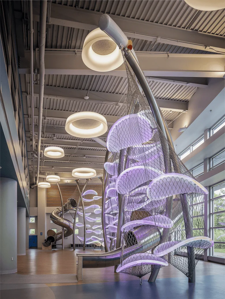 Looking up the full height of the climber, purple lit platforms stacked between curved steel ribs and ring pendant lights