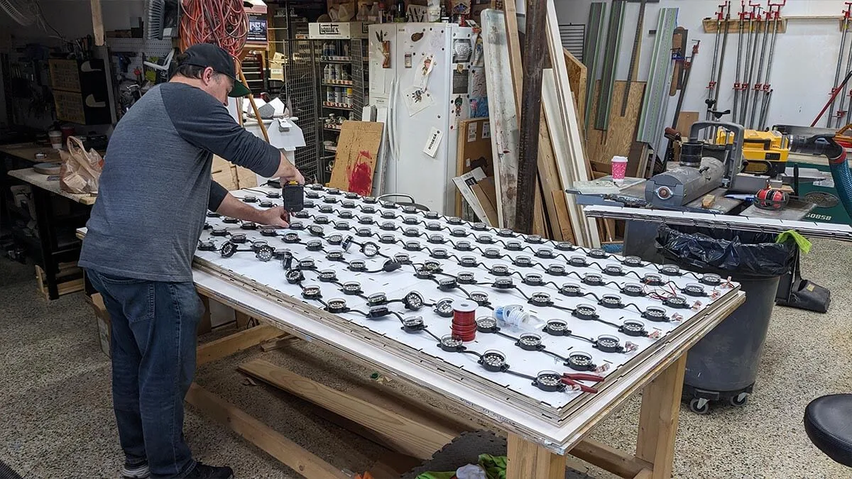Fabrication in the workshop, a maker drilling into a white panel laid across trestles with rows of LED dots already fitted