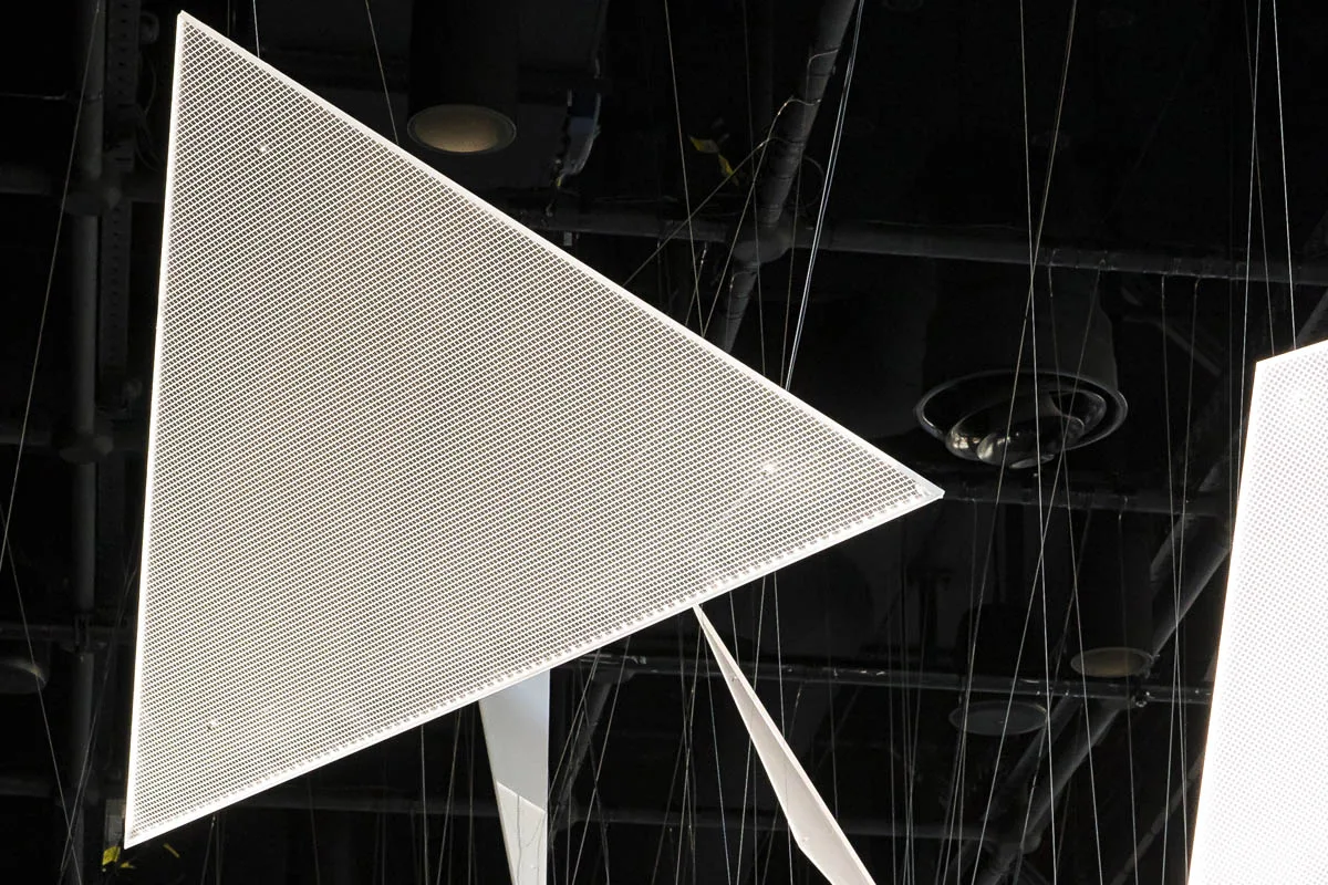 One large triangle lit from its edge, the fine v-cut grid visible across the surface against the black ceiling