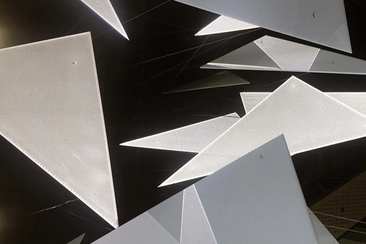 A tight cluster of overlapping triangles lit from above so their edges catch and the dark ceiling drops away