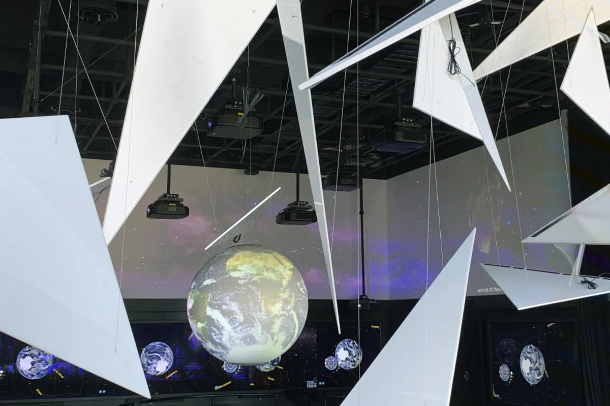 Triangles suspended in front of the round globe screen, its projected Earth glowing in the darkened gallery