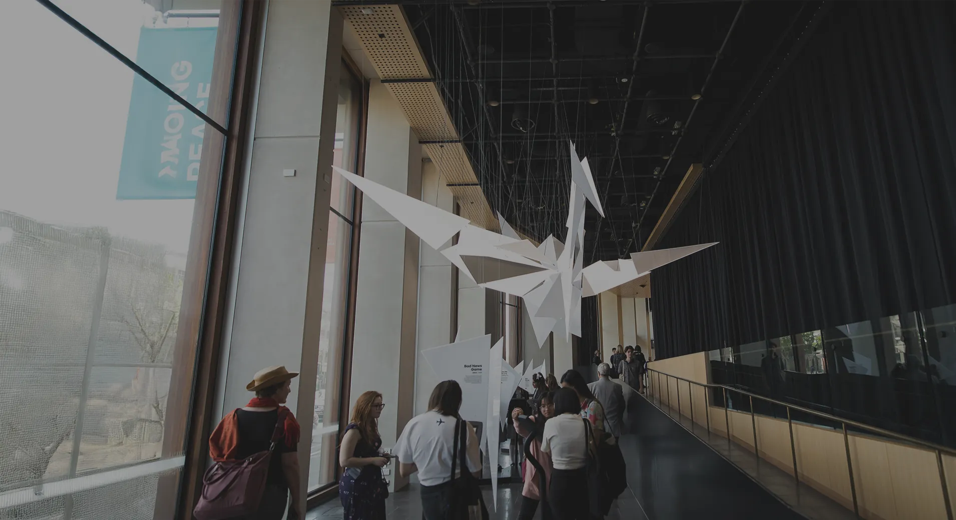 The folded white crane forms suspended over a museum walkway, visitors passing beneath them along the glazed upper level