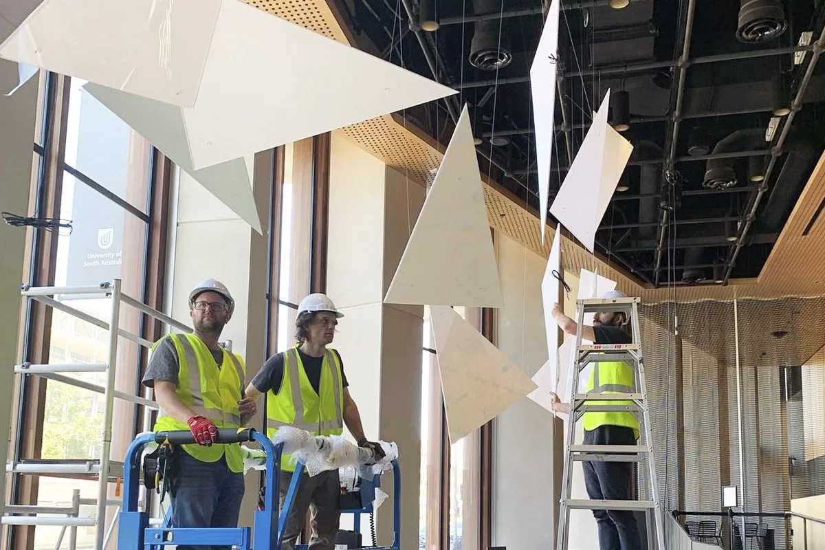 Two installers in hi-vis on a blue scissor lift with a third up a step ladder, panels part-hung above them