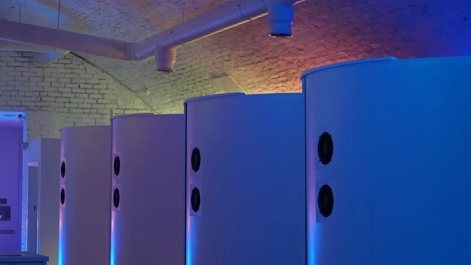 Row of pod backs seen along the side wall, blue light spilling from their bases onto the painted brick