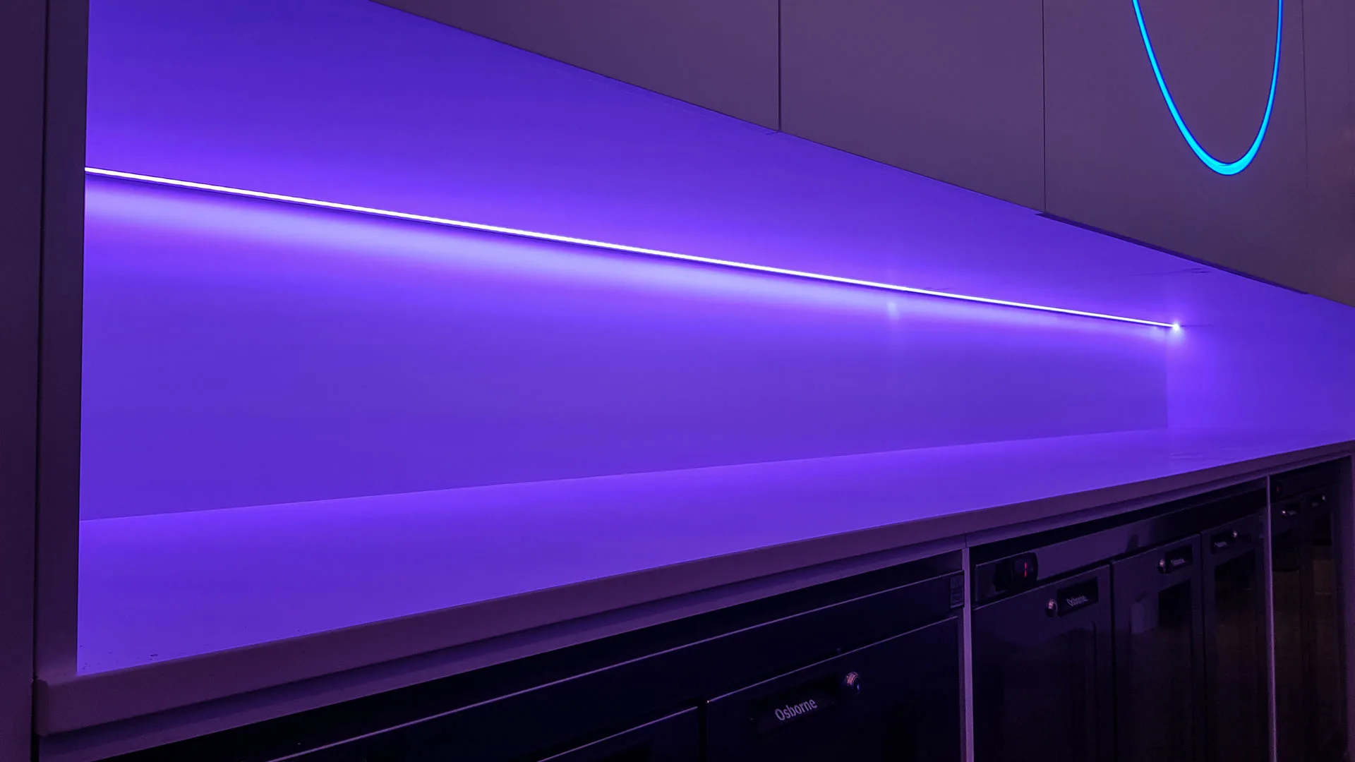 A single recessed LED line grazing the violet back wall of the bar, a blue neon arc on the panel above