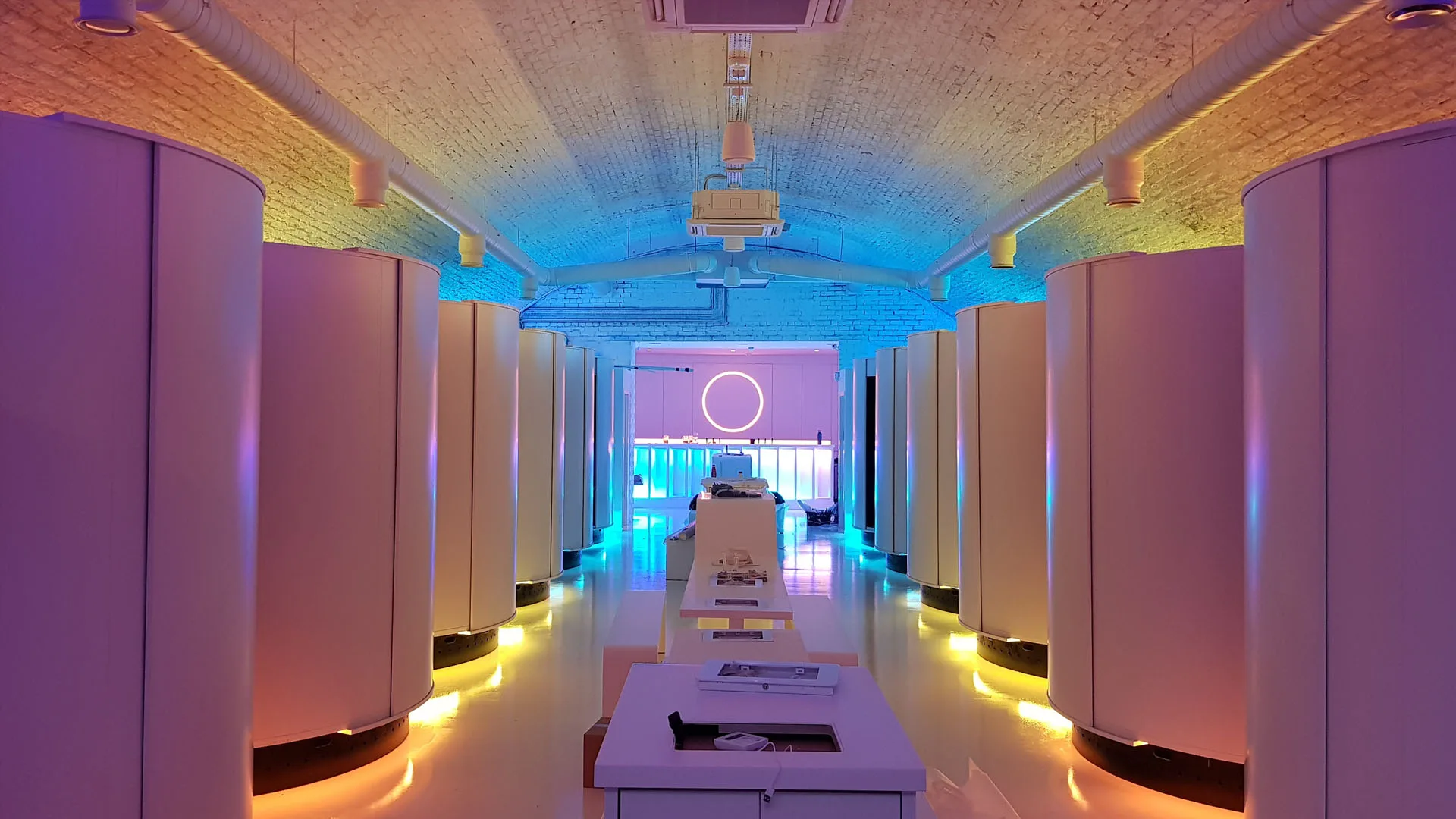 Full length of the pod arch with white service counters down the centre and the neon ring above the bar at the end