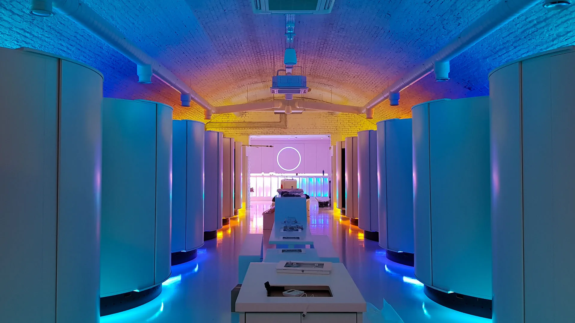 The same arch lit cool blue with amber grazing the brickwork, the white neon ring glowing over the bar at the far end