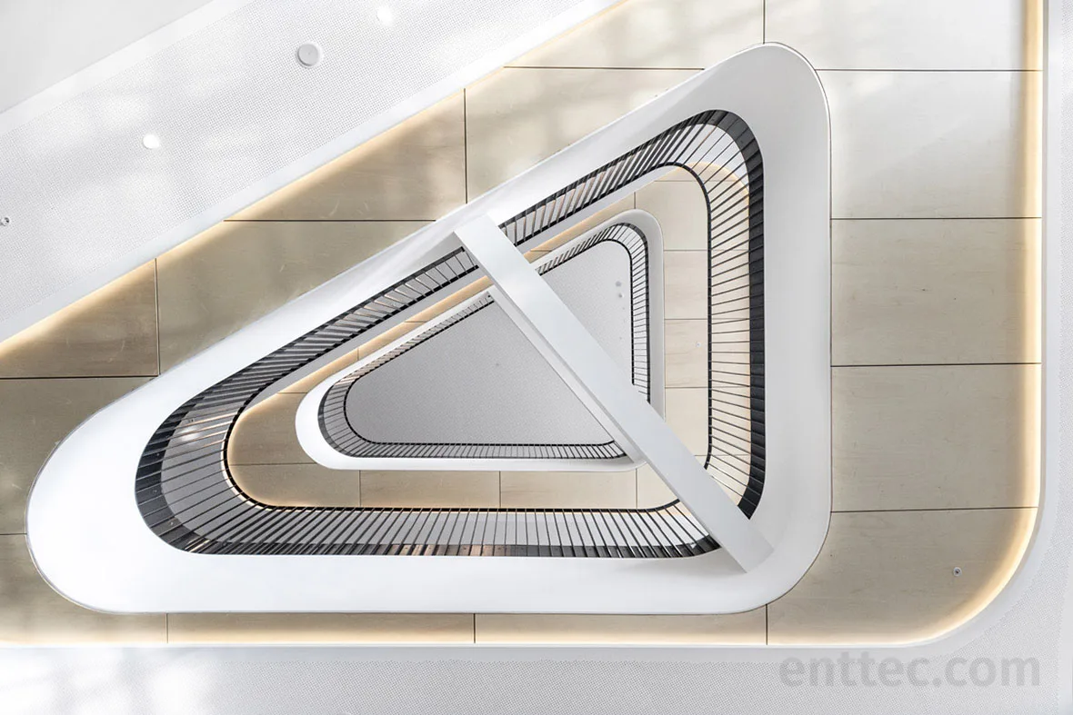 The full triangular stair void from the top landing, every level rimmed with LED tape and a white beam crossing the opening