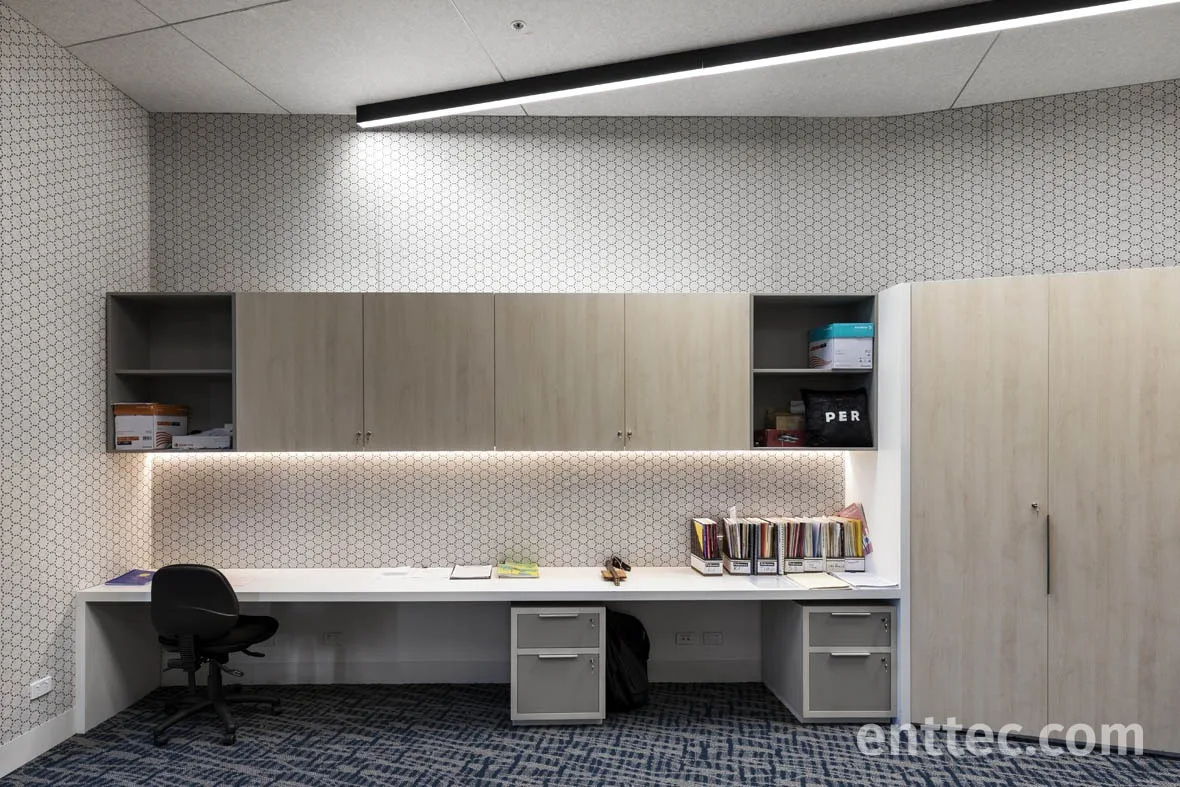 Staff work room with a long white desk run, warm LED tape under the overhead cupboards and a linear fitting above