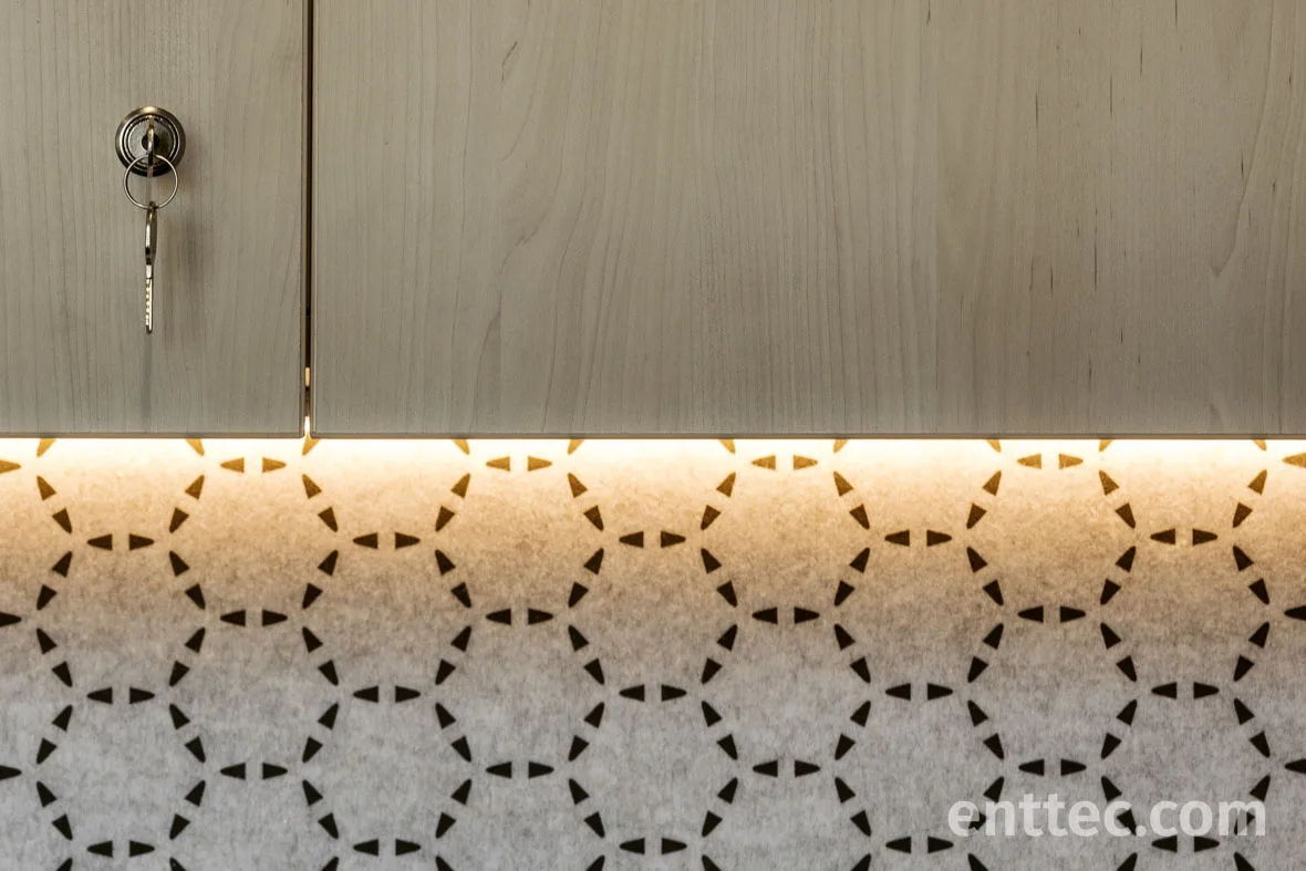 Close up of warm LED tape under a timber cupboard washing the perforated grey acoustic panel below, a key left in the lock