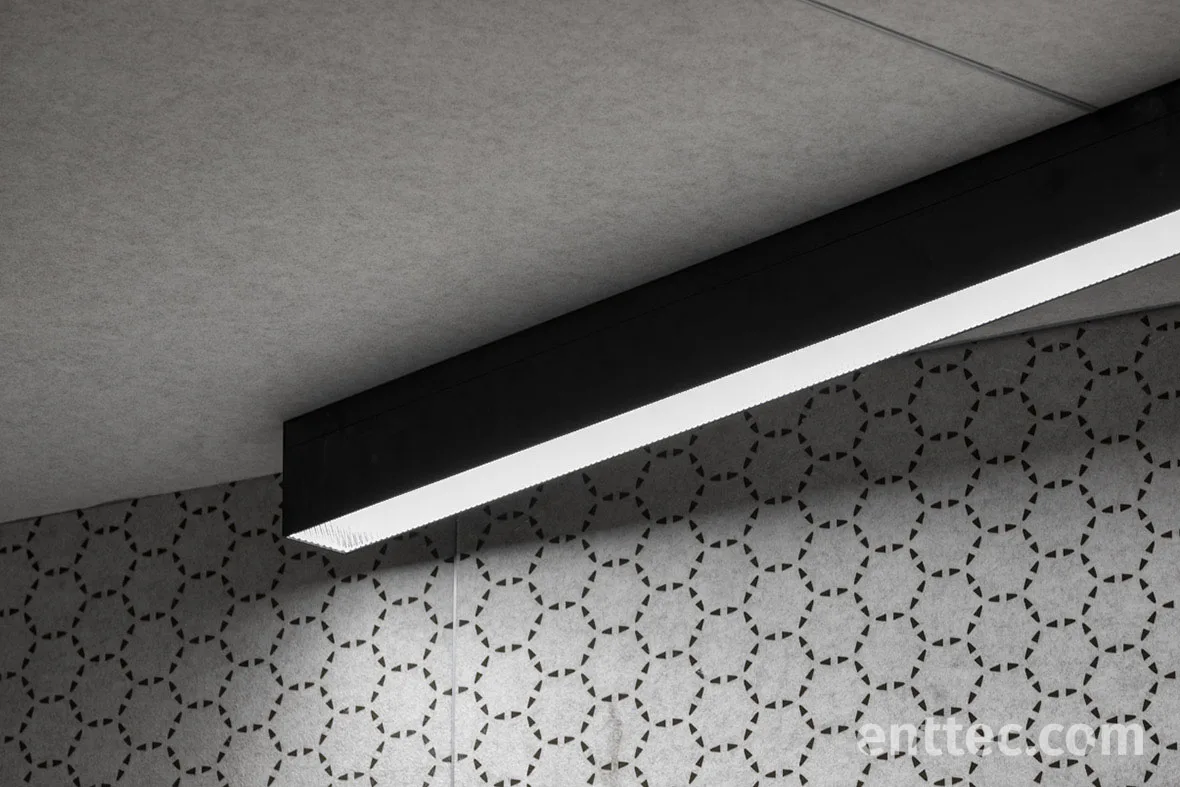 Looking along the black ceiling channel and its white linear luminaire, the hexagon acoustic wall running away beneath