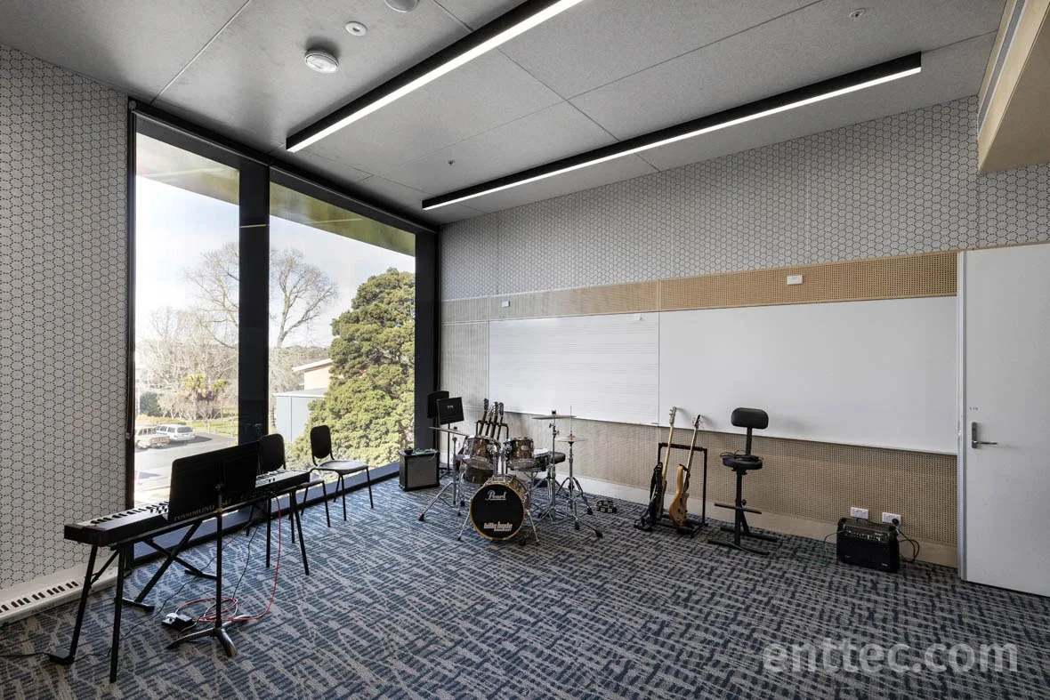 Music room set up with a keyboard, drum kit and stools, a tall window looking out to trees
