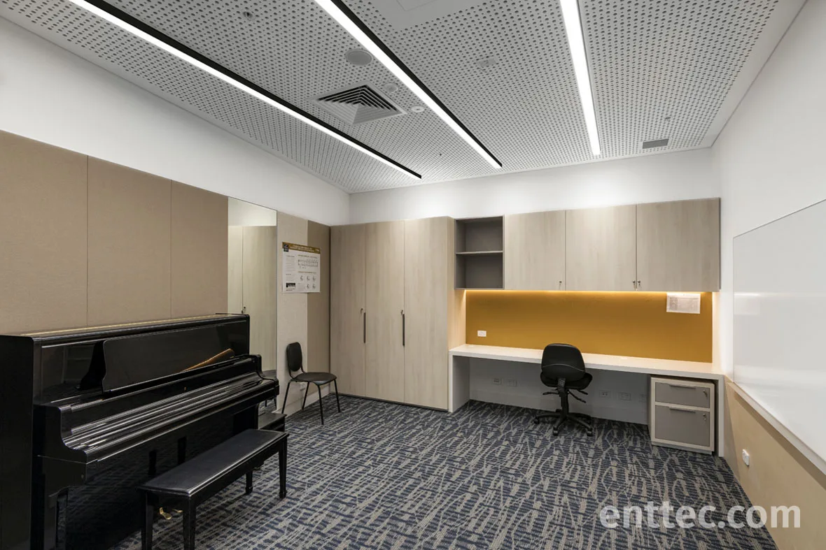 Practice room with an upright piano and a built-in desk, amber light glowing from the recess above the worktop