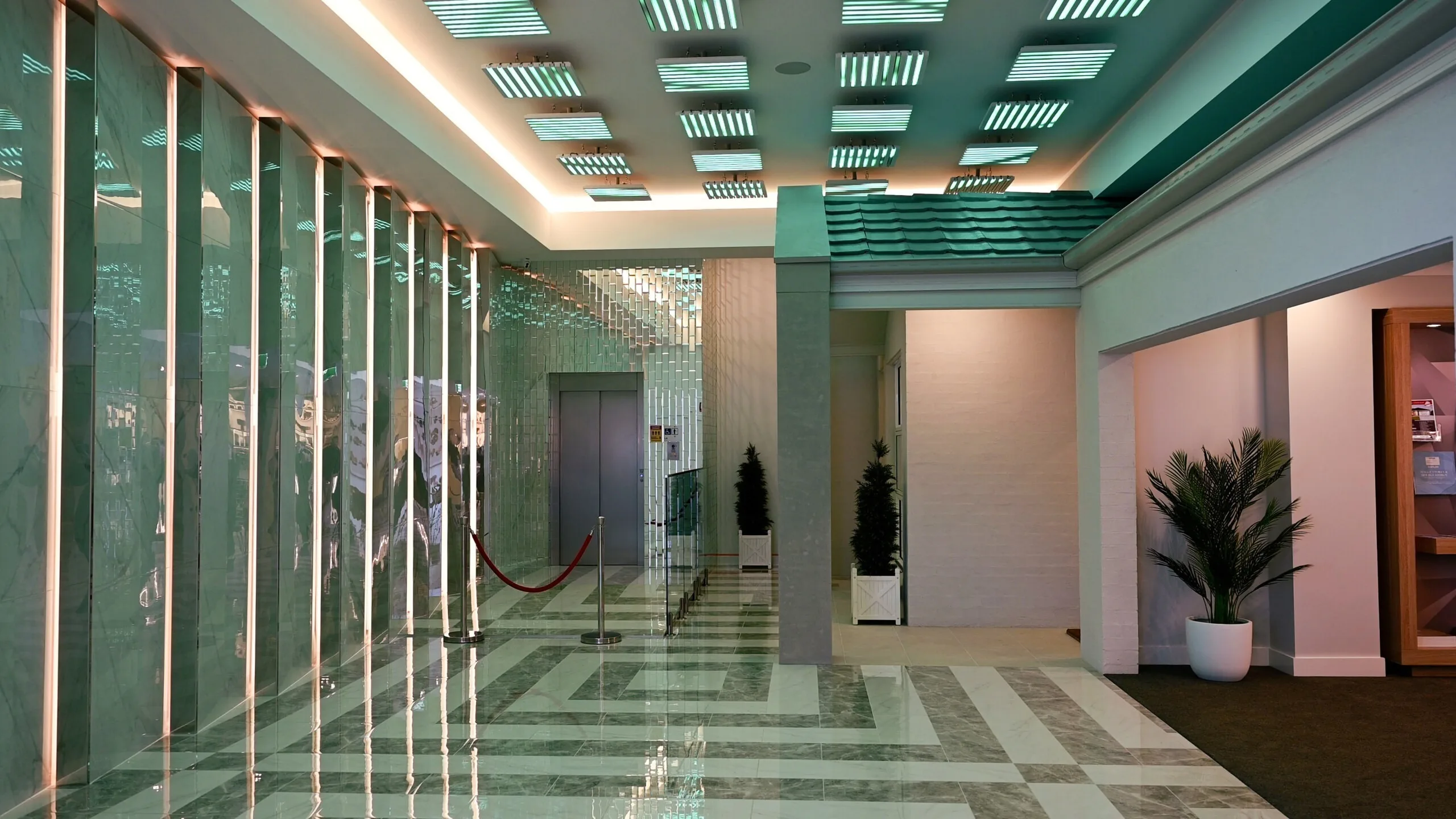 The same lobby in teal, looking down the mirrored wall towards the lift doors and a red rope barrier