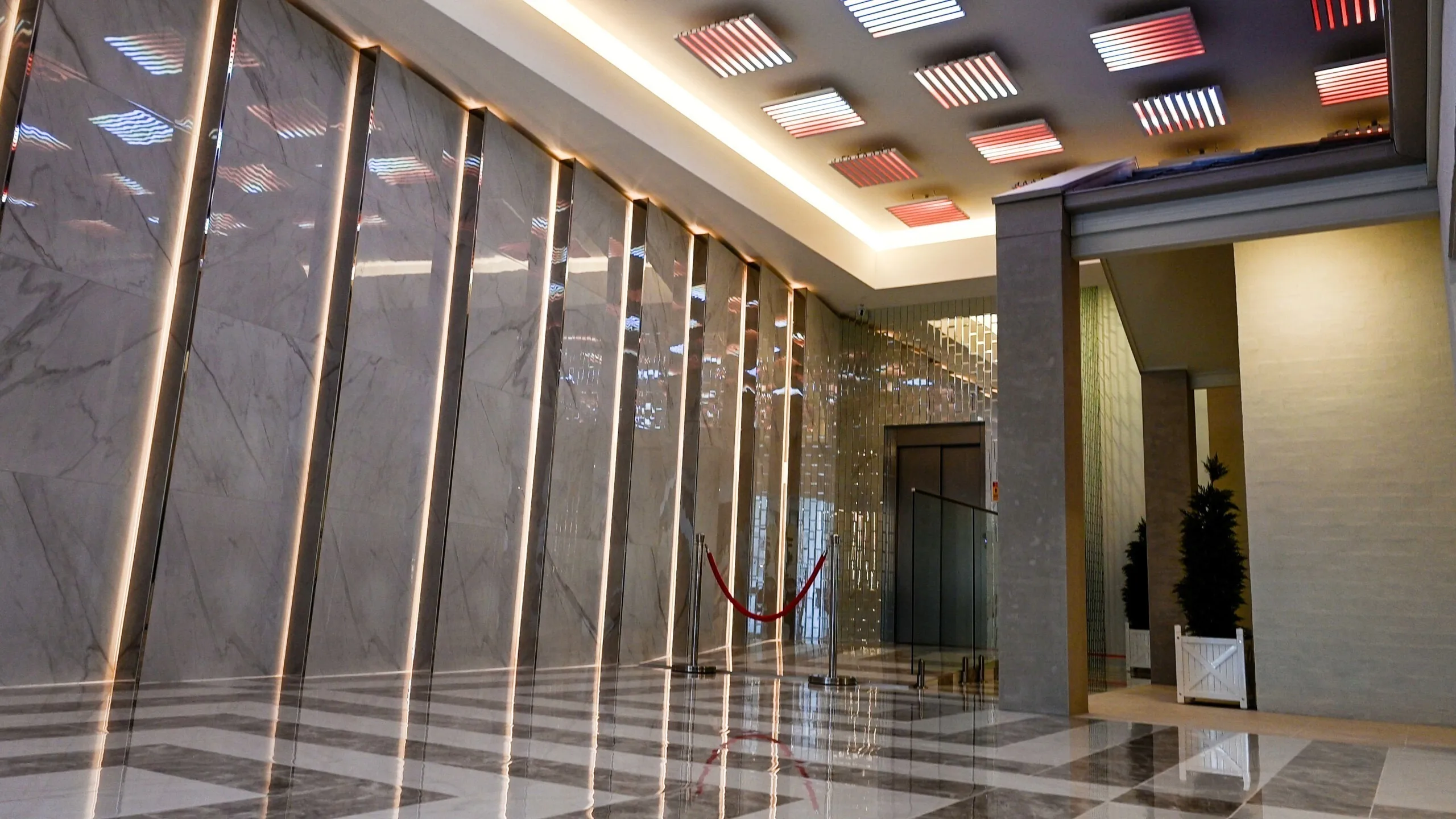 Corridor lit red and white, striped ceiling pods above a marble wall lined with vertical gold battens