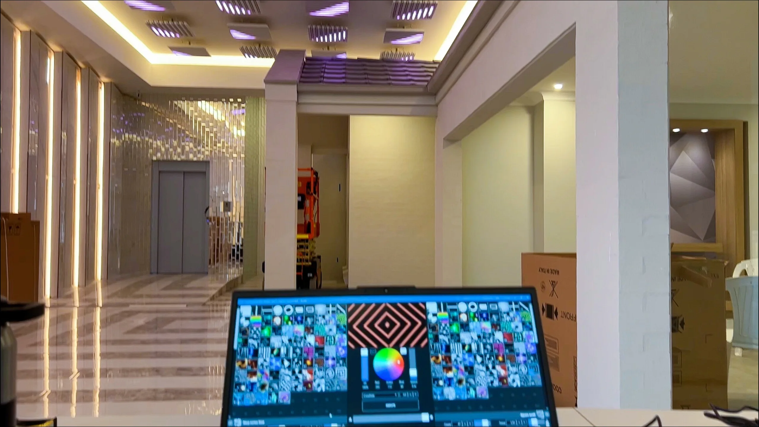 Lobby in blue and violet with a laptop and control gear on a table at right, its screen showing a grid of test colours