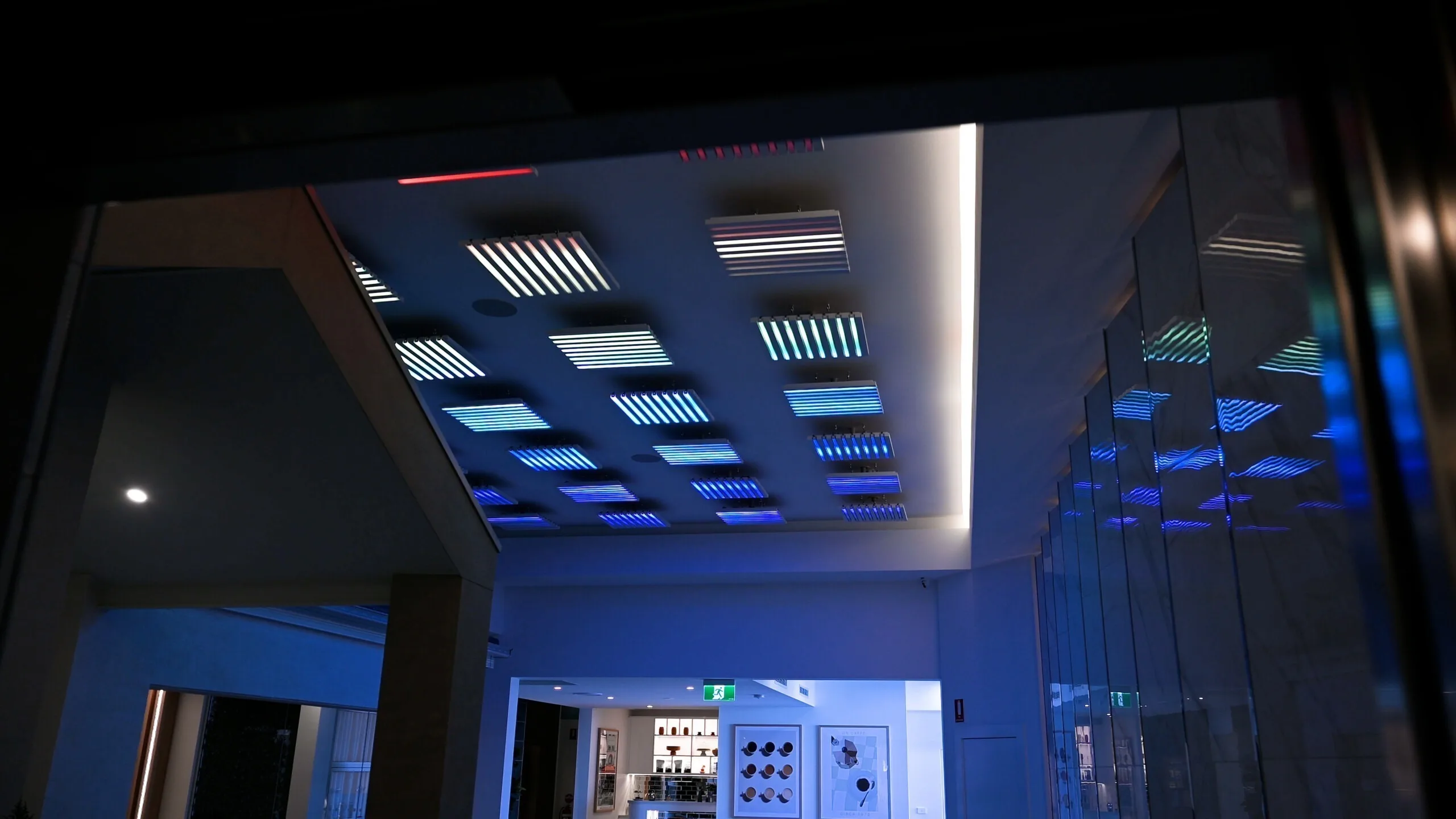 Blue and white pods glowing over a darkened lobby, mirrored glass panels on the right and a wall control panel at the far end