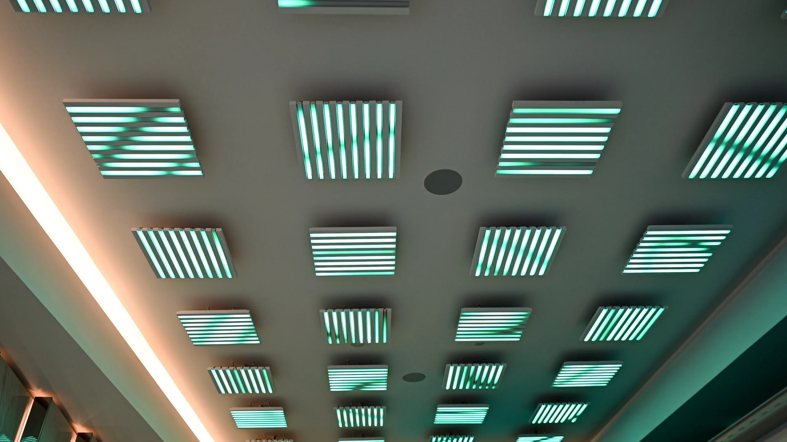 Ceiling pods in green and teal seen at an angle, warm cove lighting running along the bulkhead below them