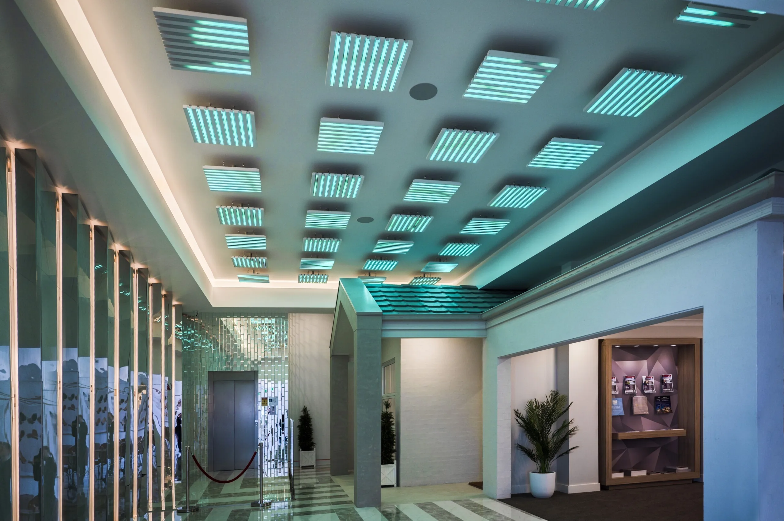 Aqua lit lobby looking towards a display home entrance, pods overhead and a planter beside the mirrored wall
