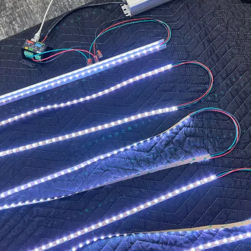 Lengths of pixel strip lit white and blue on a padded blanket during burn-in testing