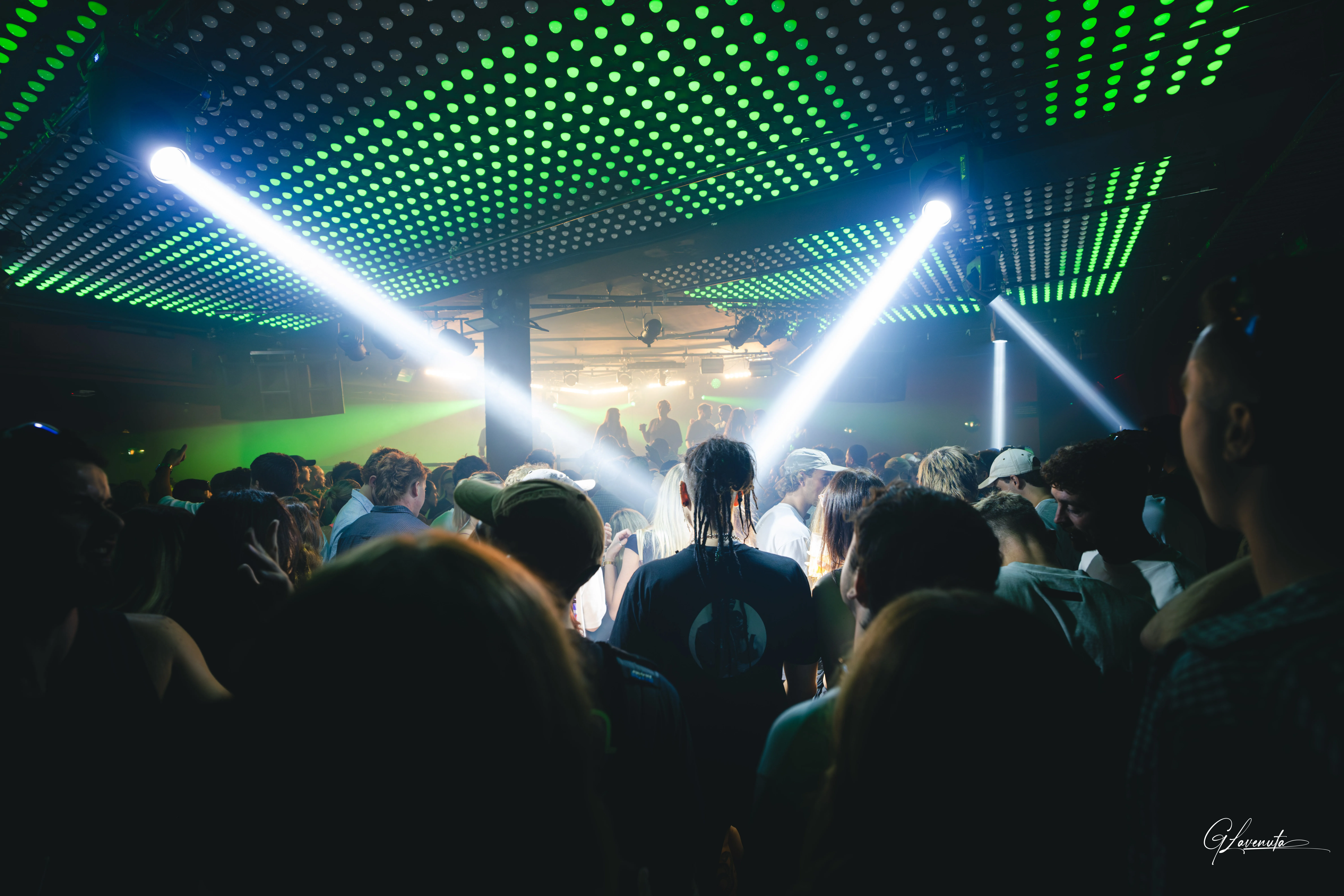 Two white beams crossing beneath the green dot ceiling, phones held up in the crowd below