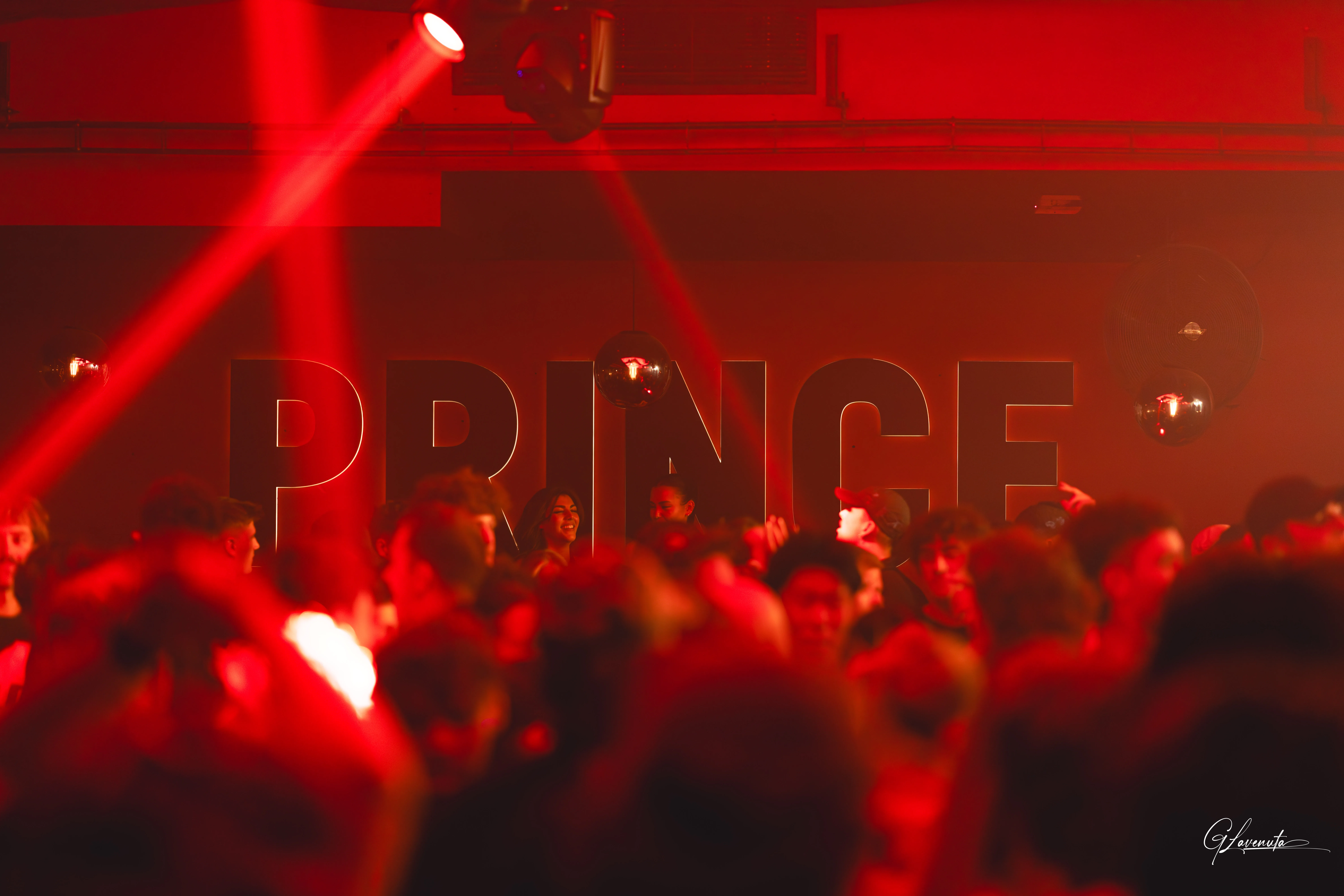 Red beams cutting through haze above the crowd, the PRINCE lettering on the back wall lit red