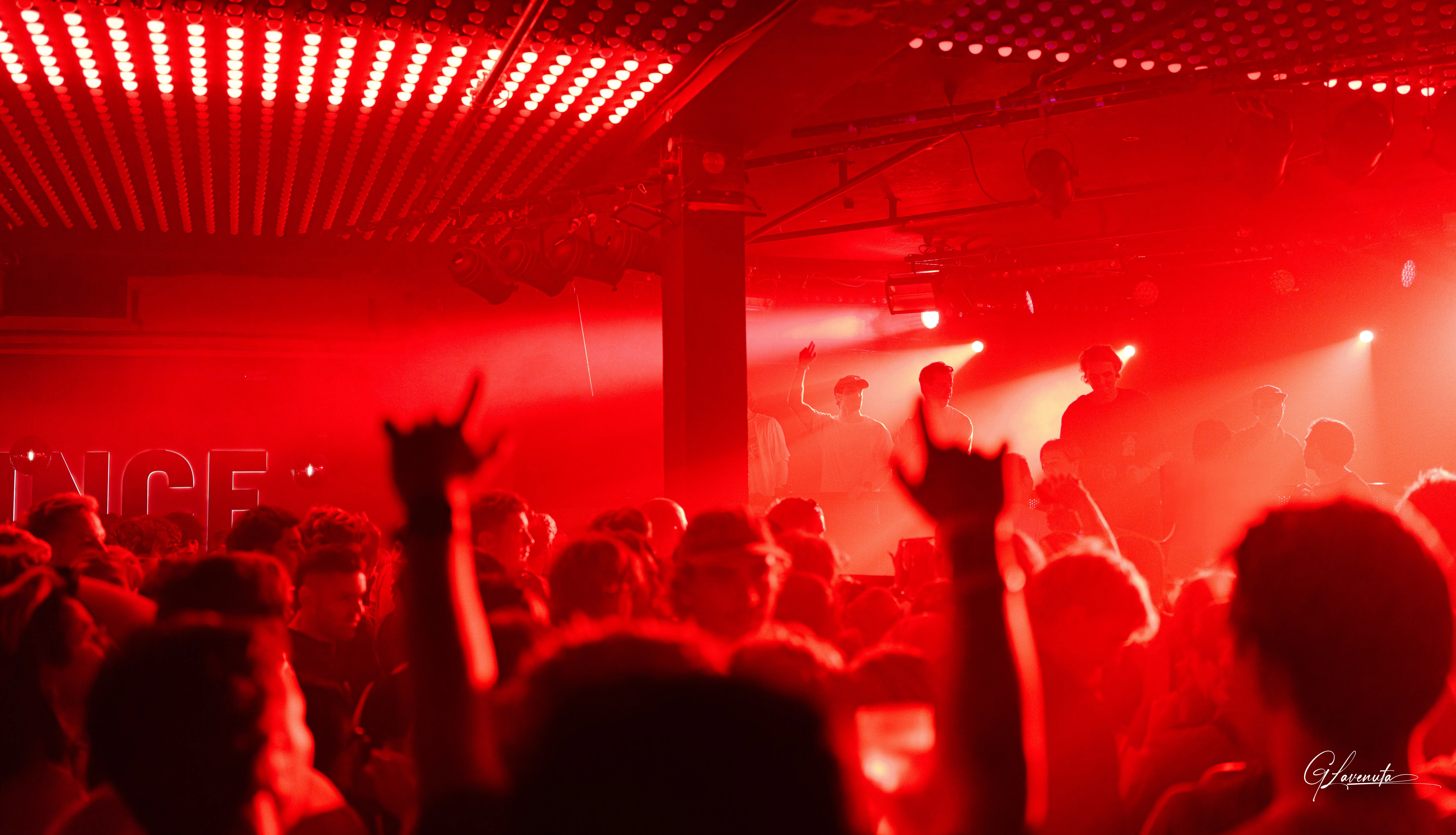 The whole room washed red, hands and horns raised under the dot grid, PRINCE lettering on the wall behind
