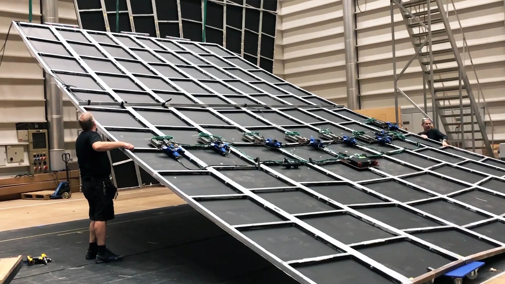 Two crew tilting a large steel grid frame off the floor, injectors already mounted along its ribs