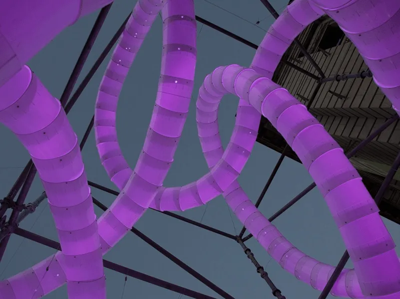 Looking up close at the tubes lit magenta, individual bucket segments and the steel frame visible against a pale sky