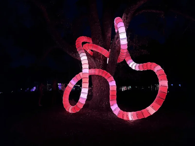 Tubing around a tree lit deep red and pink against a black night background, the trunk picked out in the glow