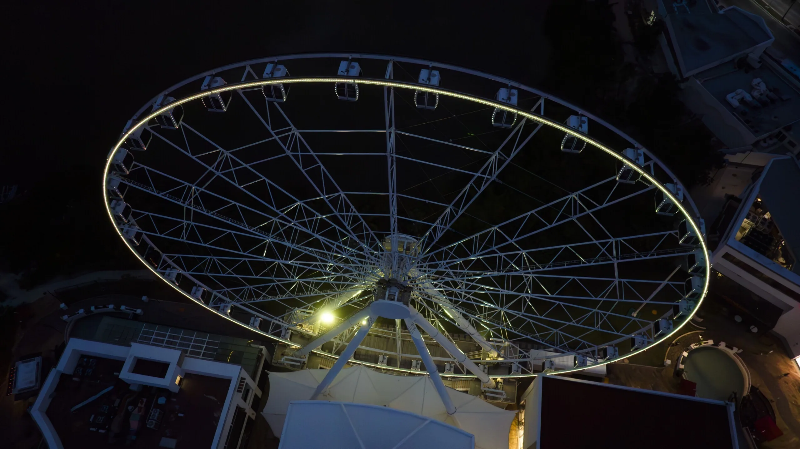 Looking almost straight down at the wheel, the rim outlined in warm white with the spokes and gondolas dark against the rooftops