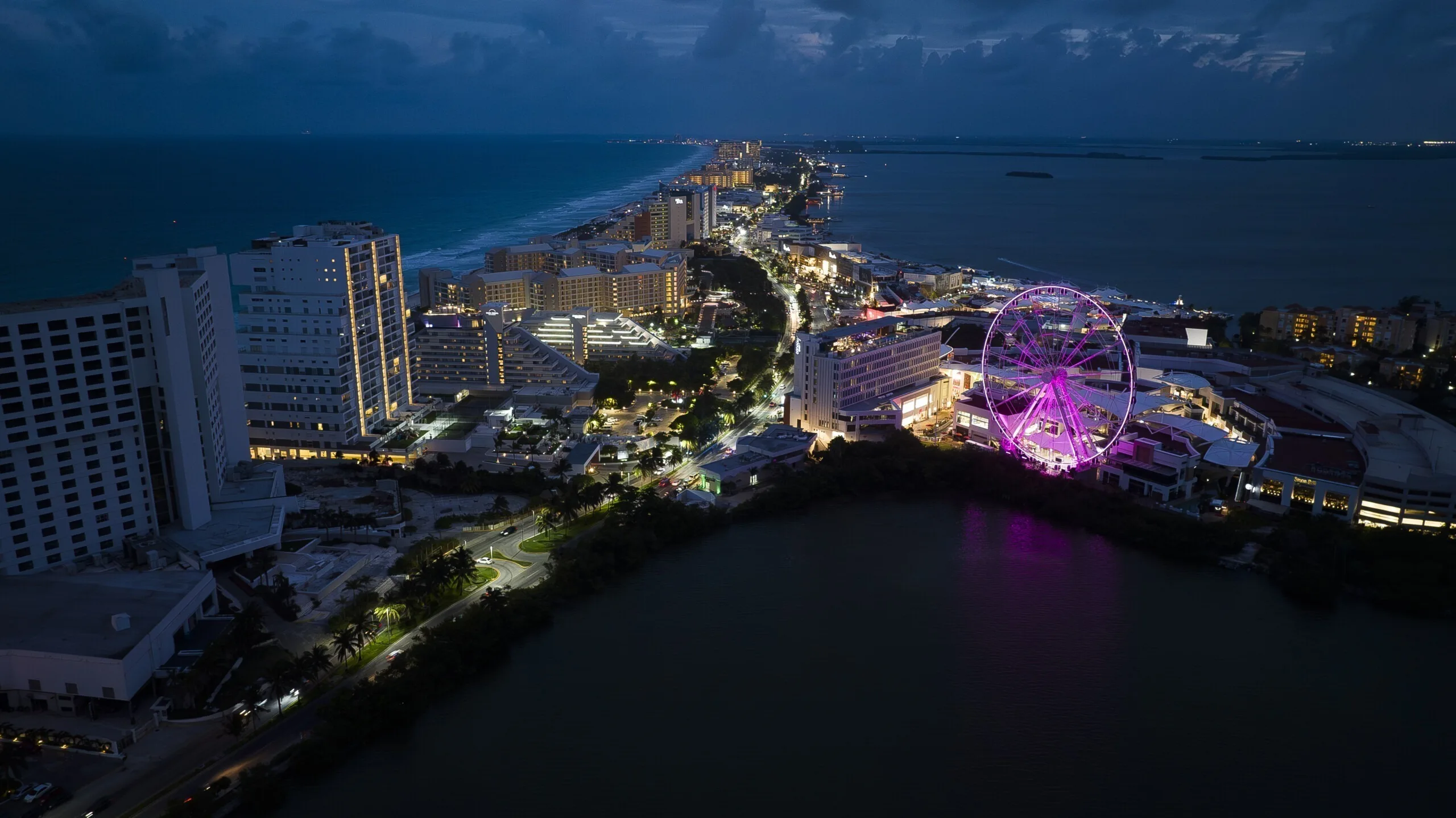 The wheel lit magenta, seen across the water with the hotel strip and open sea in the distance