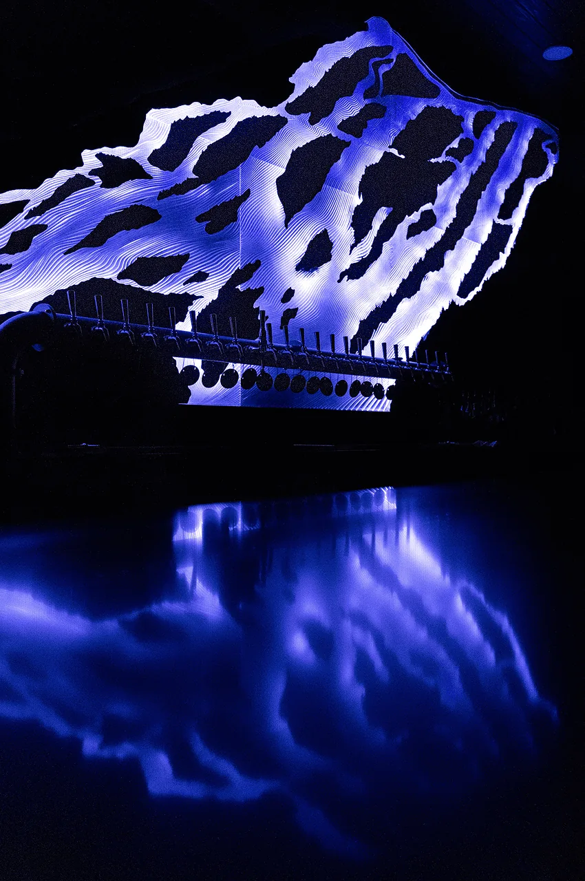 The sculpture lit deep blue and mirrored in the polished bar top below