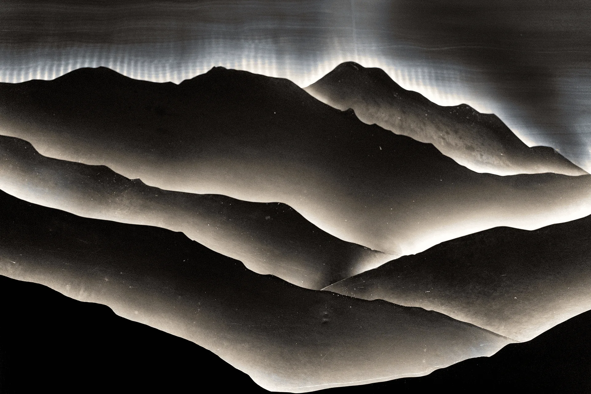 The layered steel and acrylic topography unlit, reading as a relief of mountain ridges