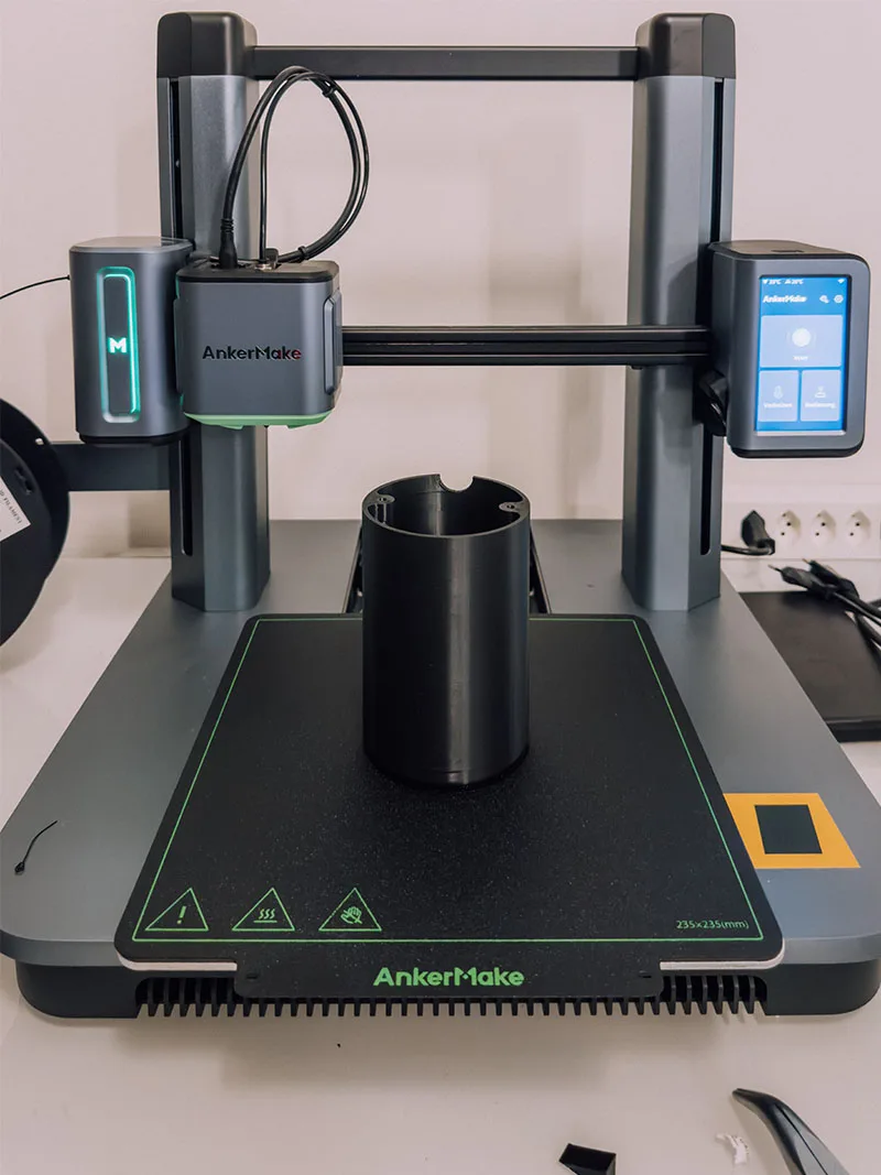 A desktop 3D printer part way through printing one of the black cylindrical canopies