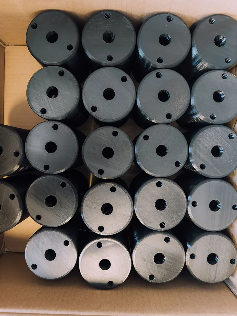 A cardboard box packed with finished black canopies stood end on, each drilled with a centre hole and two fixings