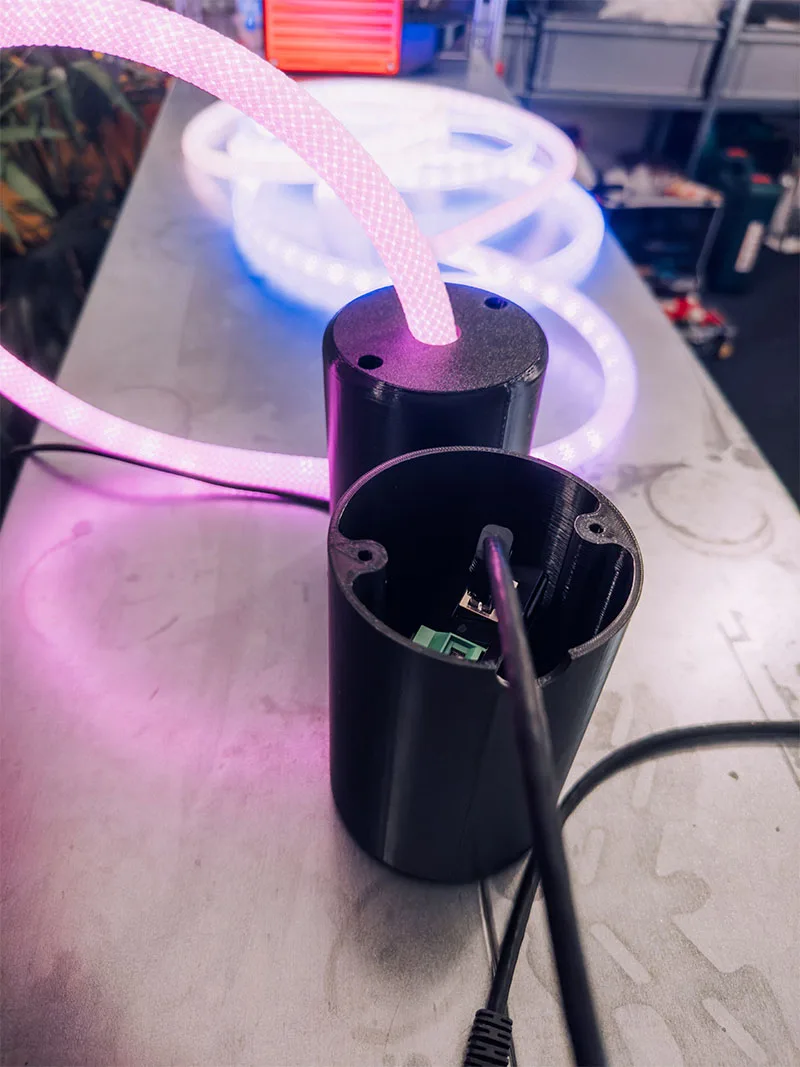 A lit light rope curving out of an open canopy on the workshop bench, the tube glowing pink and white