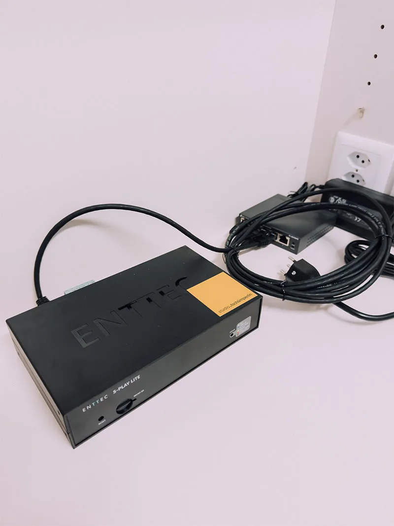 A black ENTTEC show controller wired up against a white wall, network and power leads coiled around it